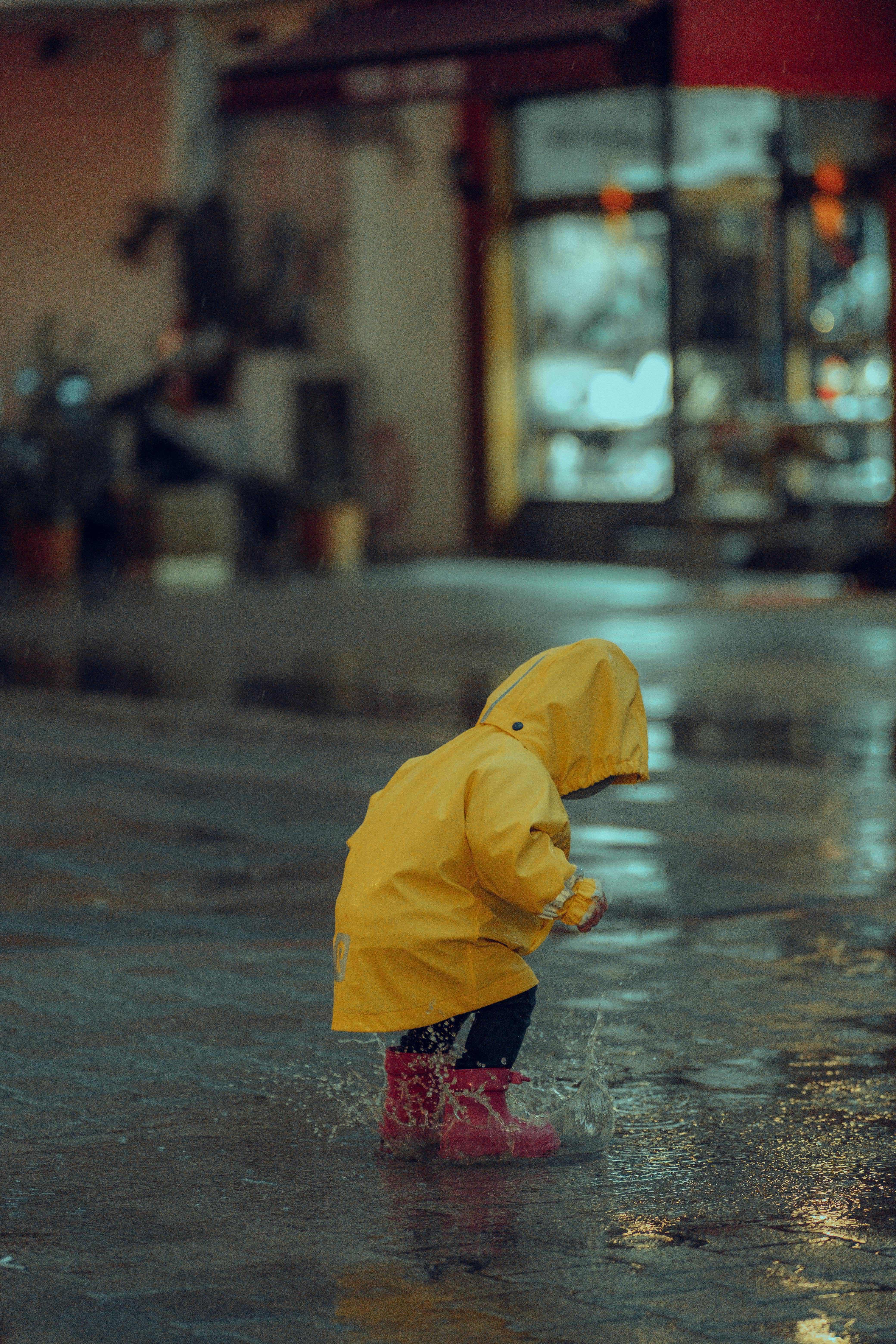 Kind in gele regenjas springt in plas